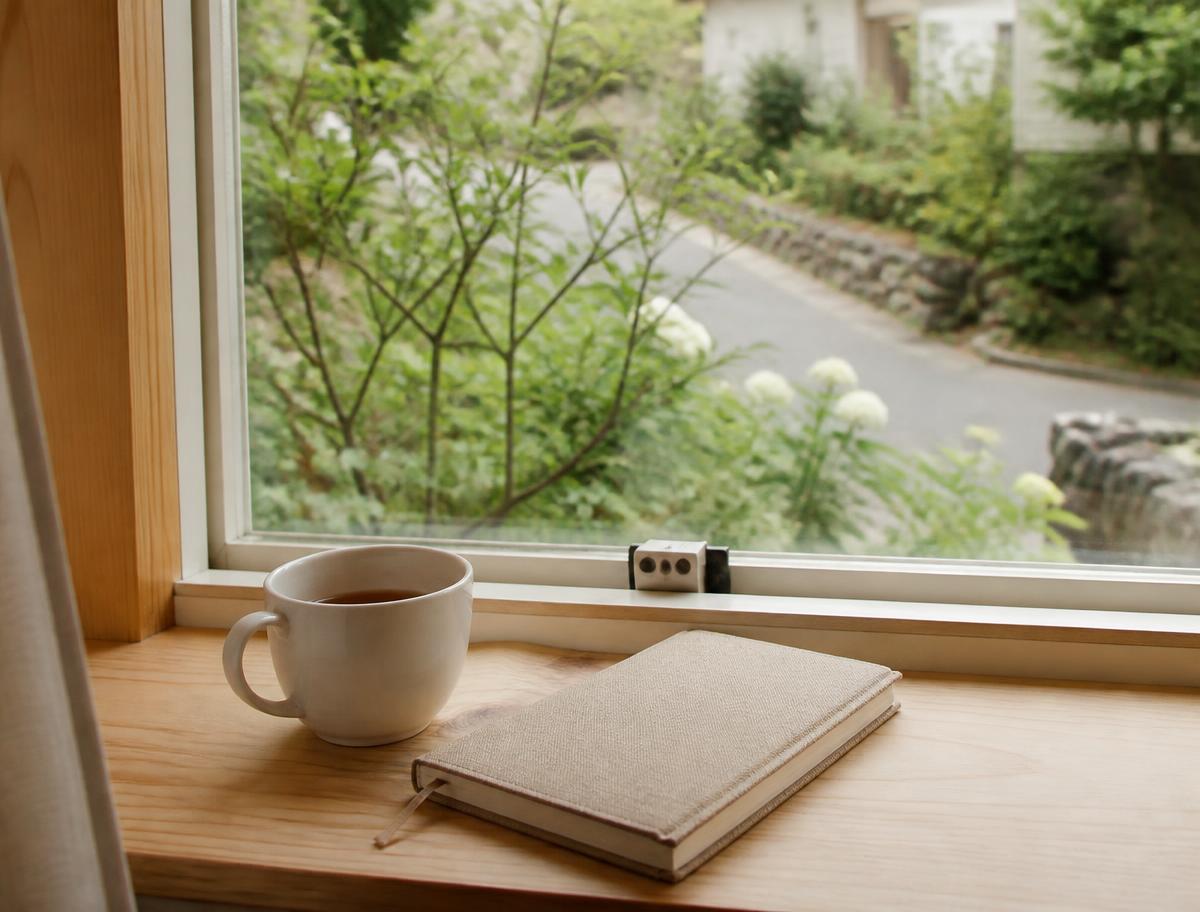 Tasse et carnet posés sur un rebord de fenêtre donnant sur un jardin calme